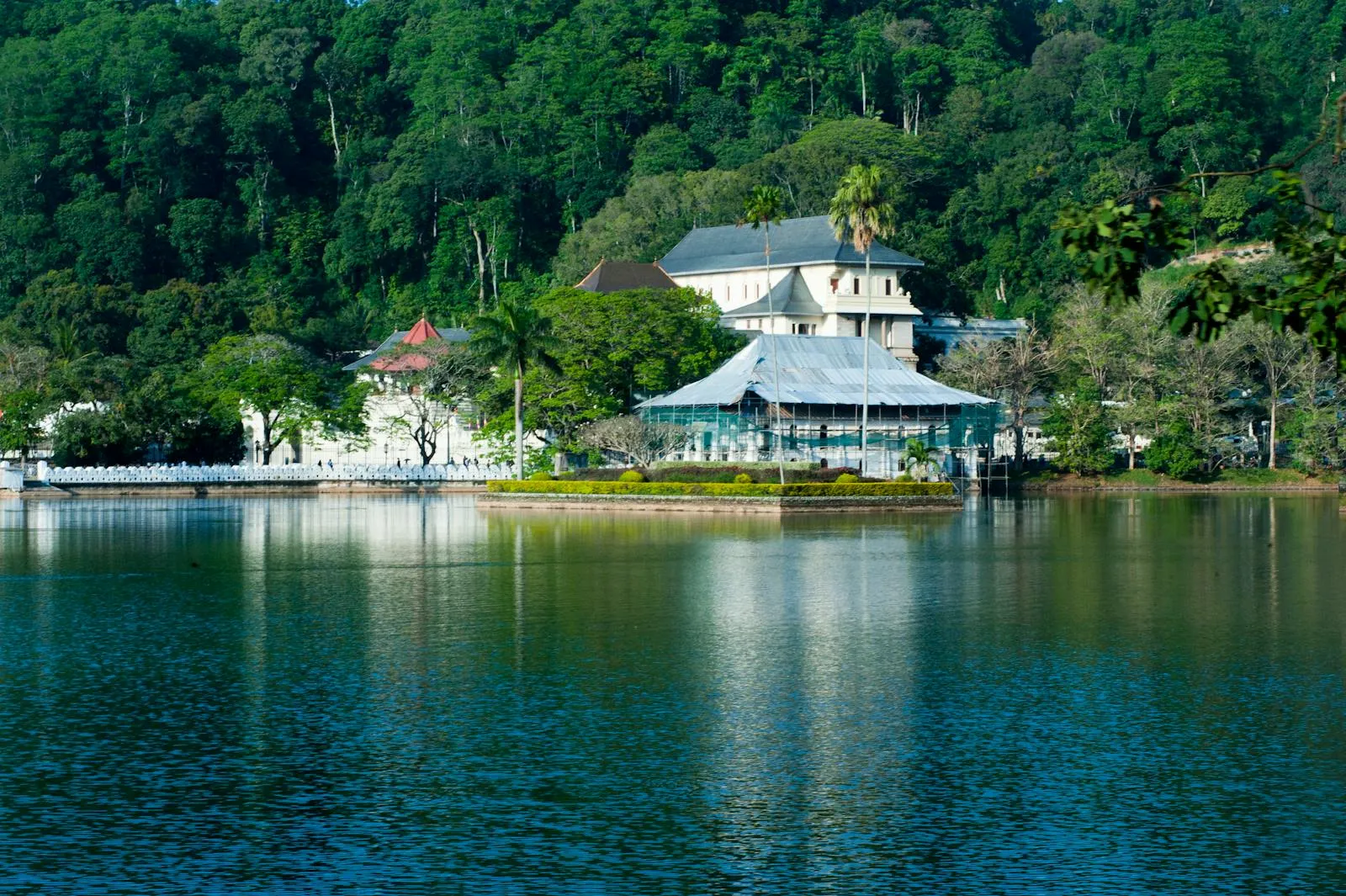 Photo by Alex P Serene view of Kandy Lake and Temple of the Tooth surrounded by lush greenery in Kandy, Sri Lanka.